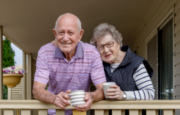 a senior couple standing on a porch while having coffee